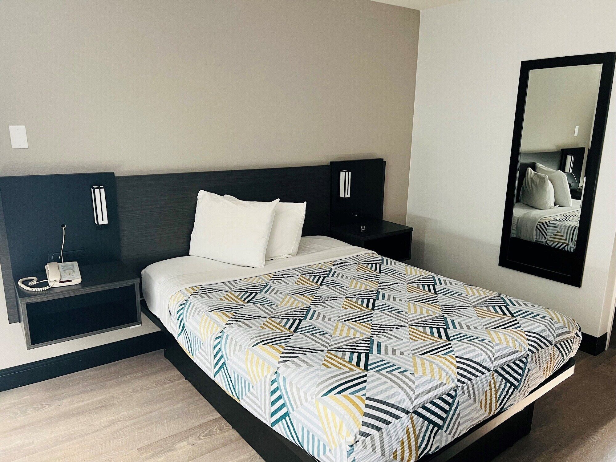 Habitación de hotel con una cama, una mesita de noche con teléfono, un espejo y televisor montado en la pared.