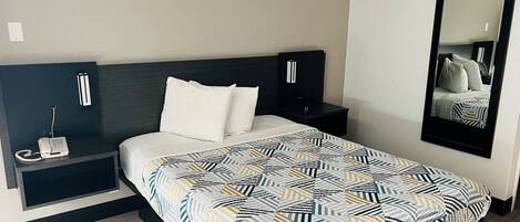 A hotel room with a bed, a bedside table with a phone, a mirror, and a wall-mounted TV.