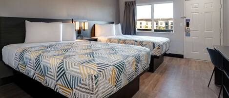 Quarto de hotel com duas camas, uma escrivaninha e vista para edifícios pela janela.