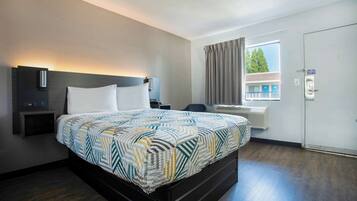 Una habitación de hotel con una cama, mesitas de noche, una ventana con cortinas y una puerta.