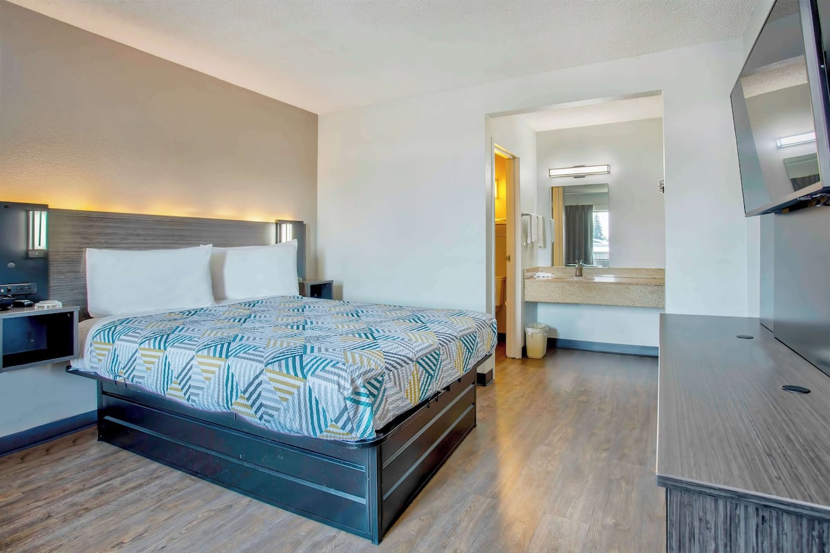 Una habitación de hotel moderna con una cama, mesitas de noche, un televisor y un baño visible a través de una puerta abierta.