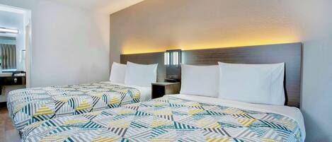 Une chambre d’hôtel avec deux lits, chacun recouvert d’une couvre-lit à motifs, une table de chevet avec une lampe et un luminaire fixé au mur.