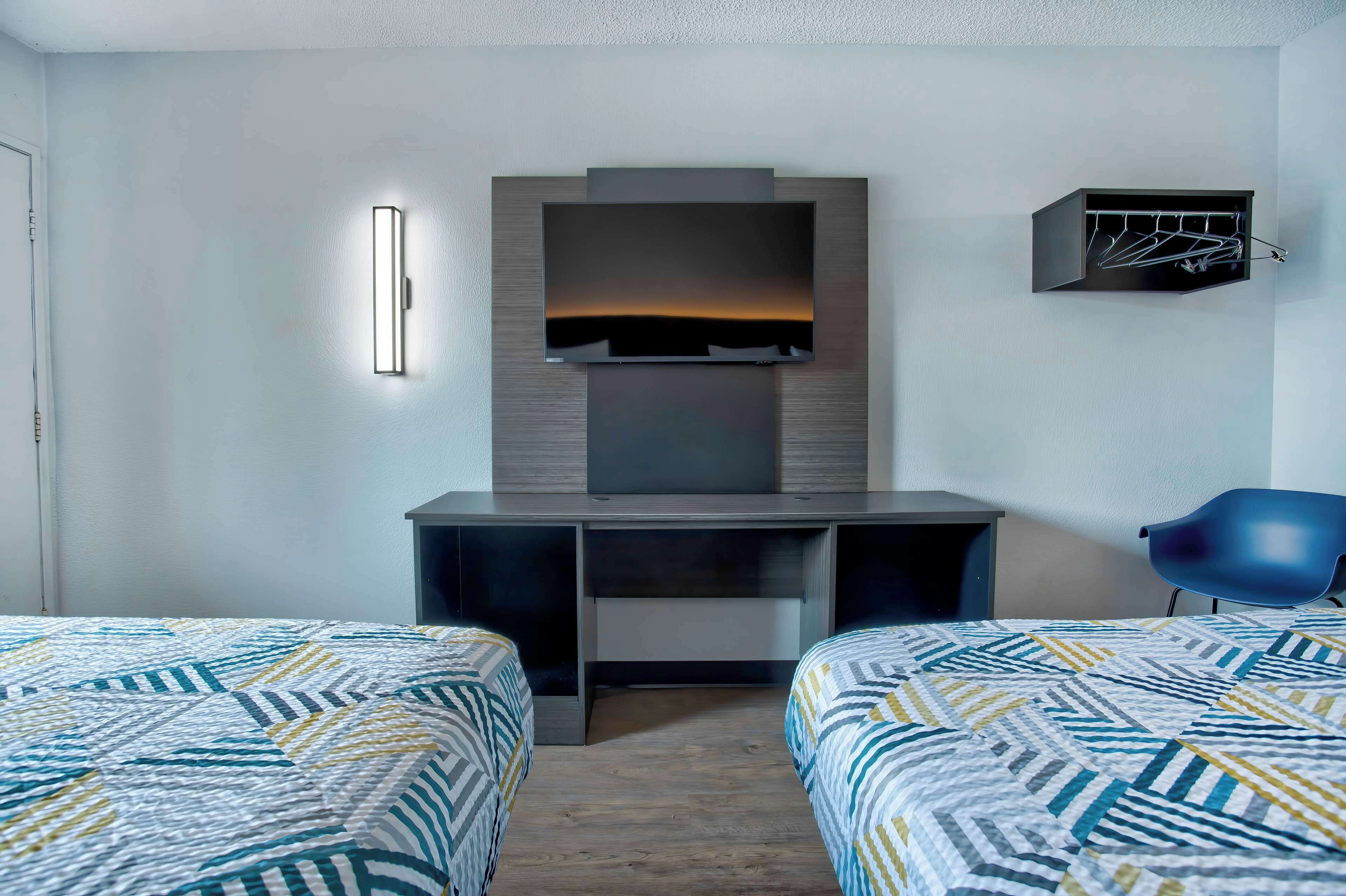 A hotel room with two beds, a desk, a TV, and a coat rack.