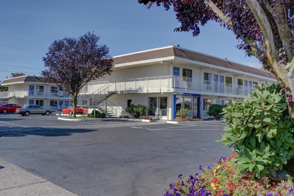 A motel with a two-story structure, a parking lot, and a tree in the foreground.
