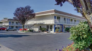 A motel with a two-story structure, a parking lot, and a tree in the foreground.