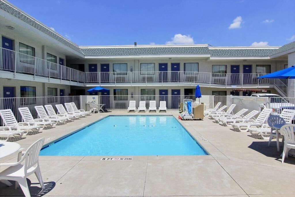 A pool area with lounge chairs and umbrellas, a building with multiple balconies, and a clear sky.