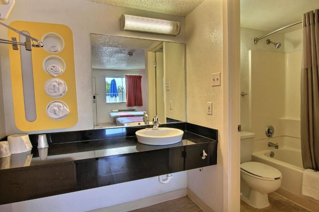 A bathroom with a black countertop, white sink, and a shower area.