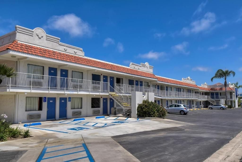 A motel with multiple rooms, a parking lot, and a clear blue sky.