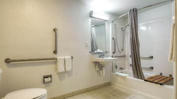 Un baño con inodoro, lavabo, ducha y barras de apoyo.