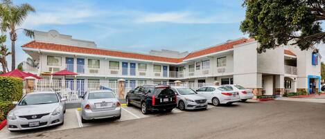 Un hotel con techo de tejas rojas, varios balcones y un estacionamiento con varios coches.