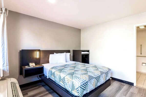 A modern hotel room with a large bed, a bedside table with a phone, and a wall-mounted light.