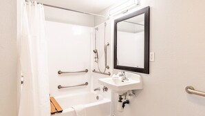 A bathroom with a bathtub, shower, and sink, equipped with grab bars and a mirror.