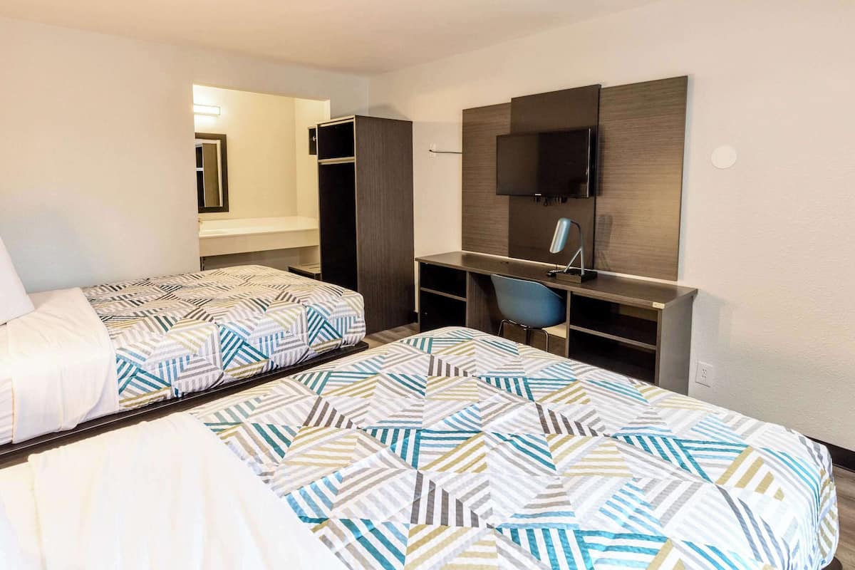 Una habitación de hotel con dos camas, un escritorio, una silla, un televisor y un armario.