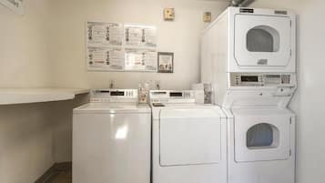 A laundry room with stacked washers and dryers, a bulletin board with informational posters, and a wall-mounted thermostat.