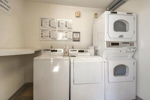 A laundry room with stacked washers and dryers, a bulletin board with informational posters, and a wall-mounted thermostat. - Motel 6 Carlsbad, CA - Near Legoland (Carlsbad)
