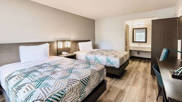 A hotel room with two beds, a desk, and a chair.
