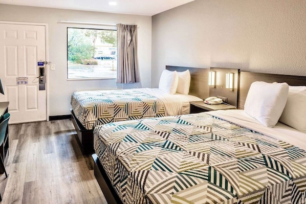 A hotel room with two beds, a window with curtains, a desk, and a telephone.