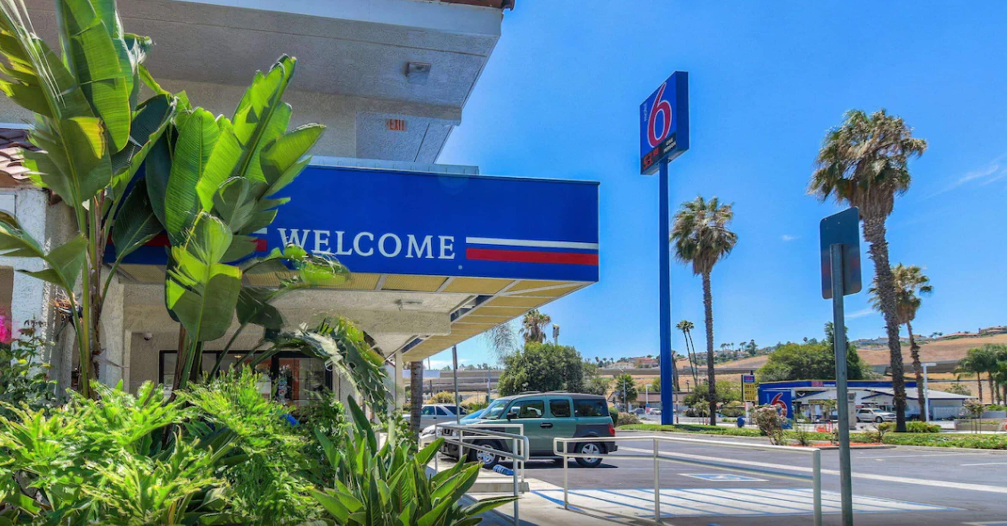 A gas station with a 'WELCOME' sign, palm trees, and a clear blue sky.