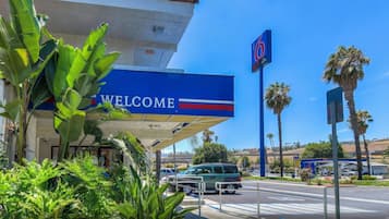 A gas station with a 'WELCOME' sign, palm trees, and a clear blue sky.