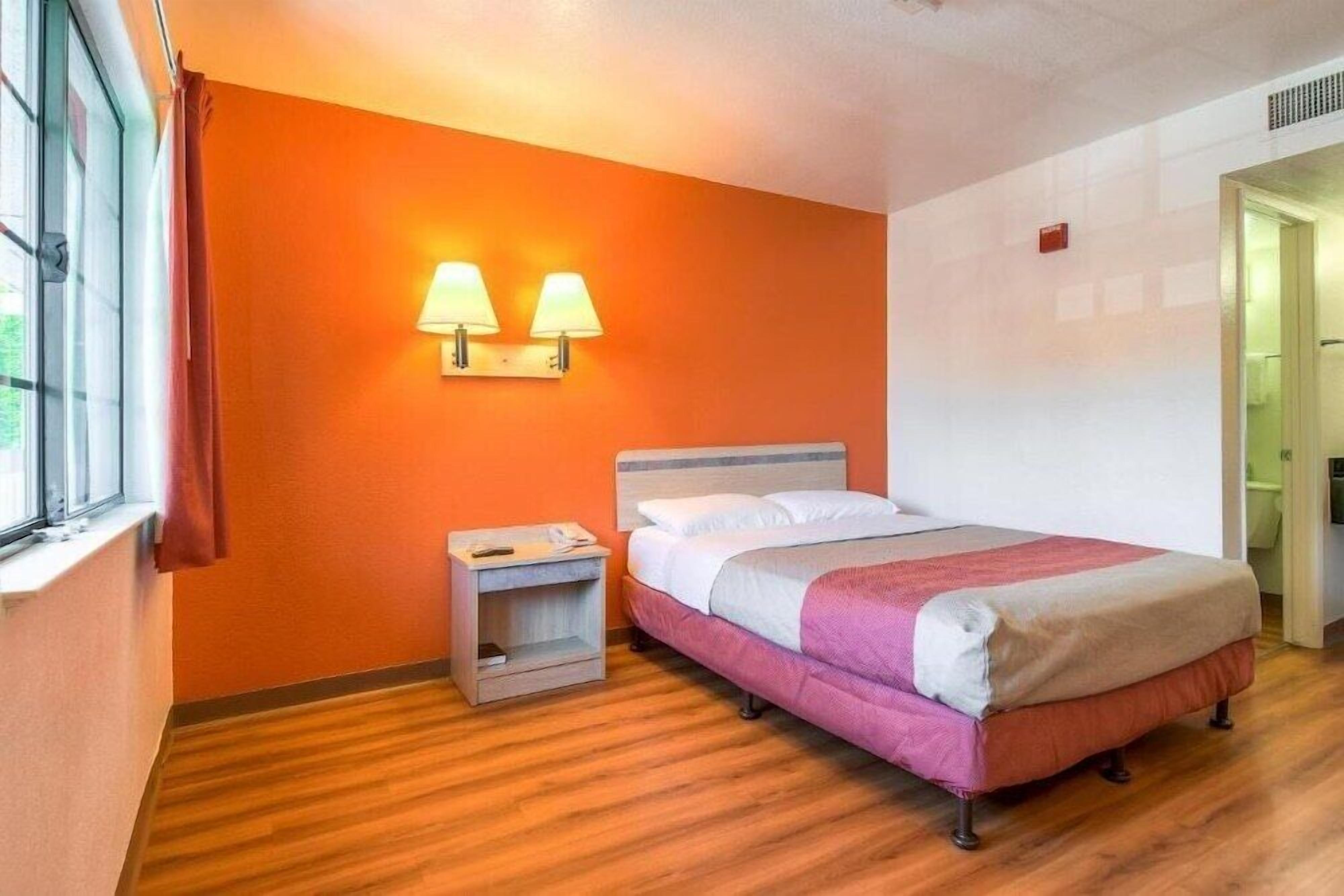 A hotel room with a bed, a nightstand, two wall-mounted lamps, and a window with curtains.