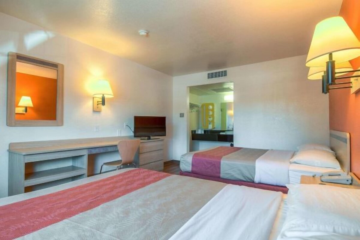 A hotel room with two beds, a desk, a chair, and a TV.