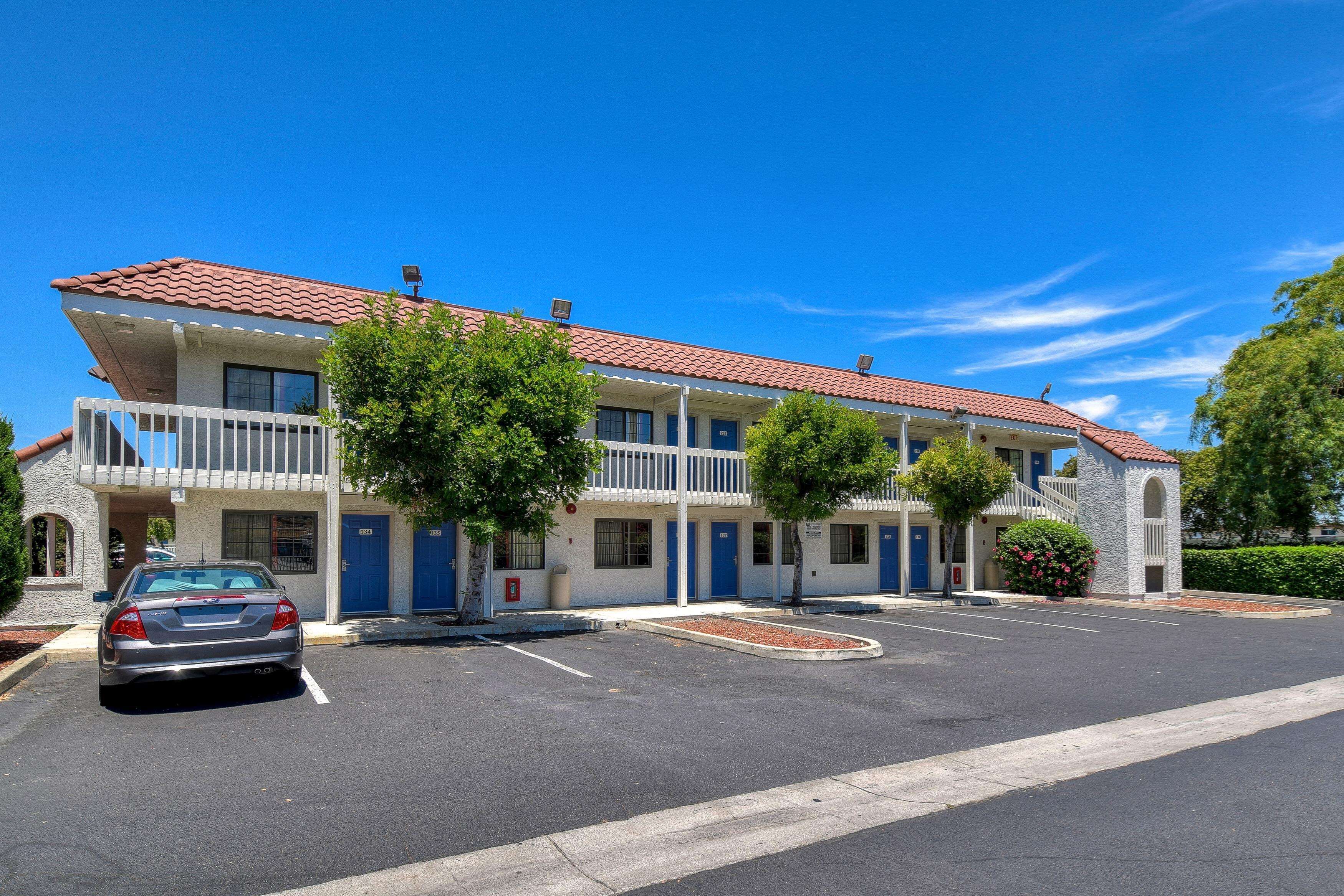 Un motel con techo de tejas rojas, varios balcones y un estacionamiento.
