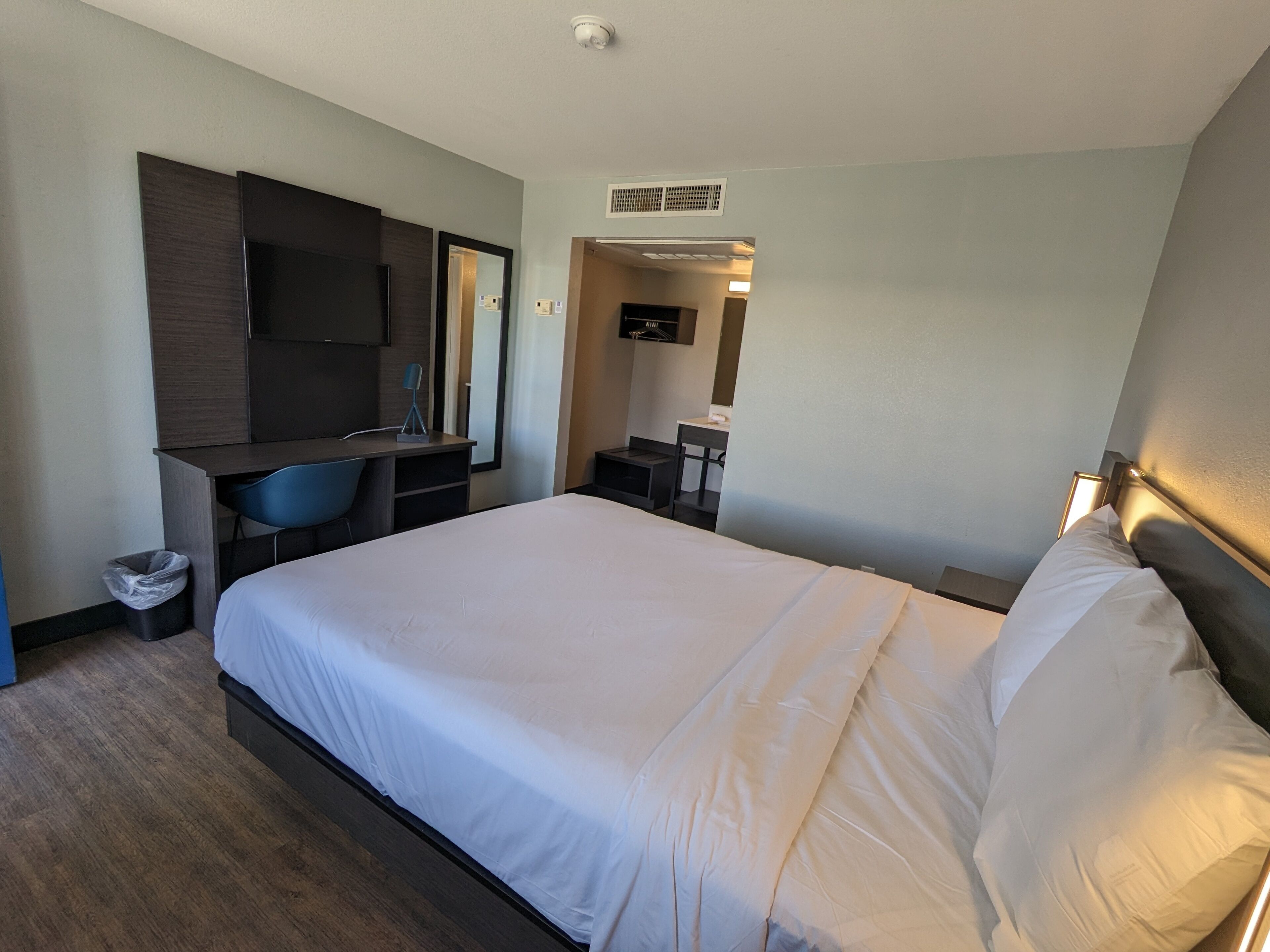 A hotel room with a large bed, a desk with a chair, a small table, and a mirror.