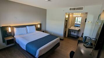 A hotel room with a bed, bedside table, lamp, and a bathroom with a sink and mirror.