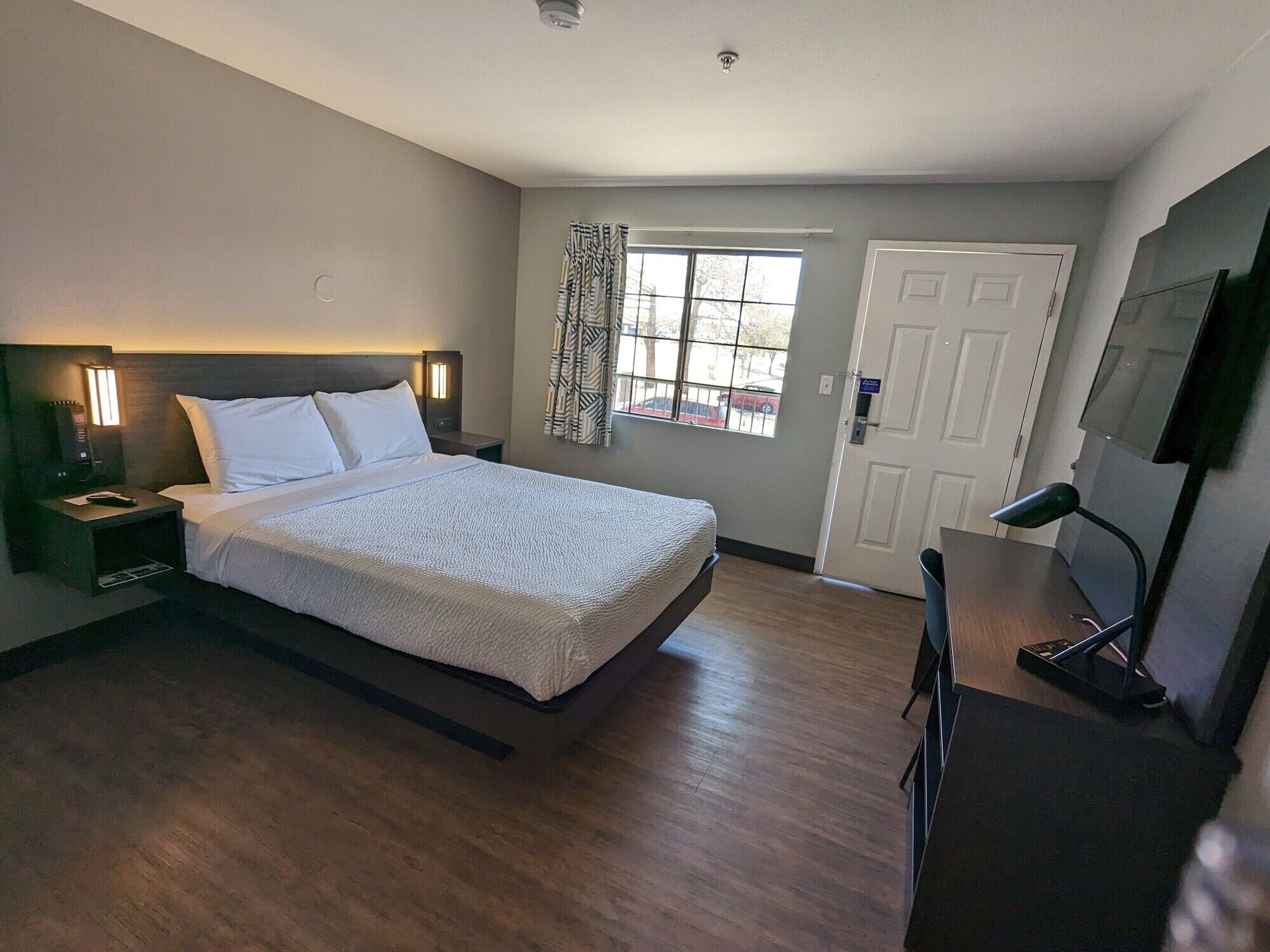 A hotel room with a large bed, bedside tables, a TV, and a window with curtains.