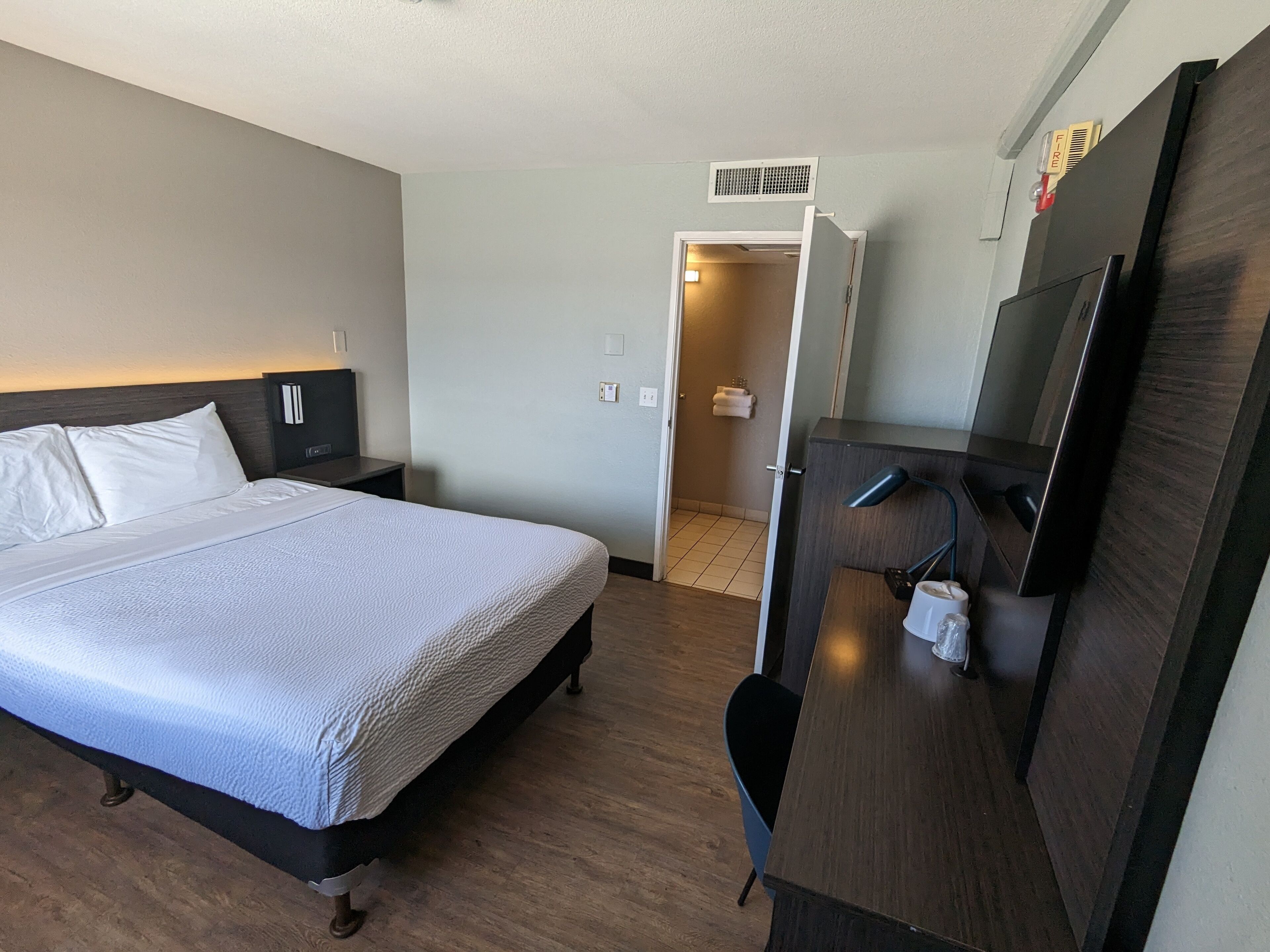 Une chambre d’hôtel avec un lit, un bureau, une télévision et une salle de bain, le tout visible à travers une porte ouverte.