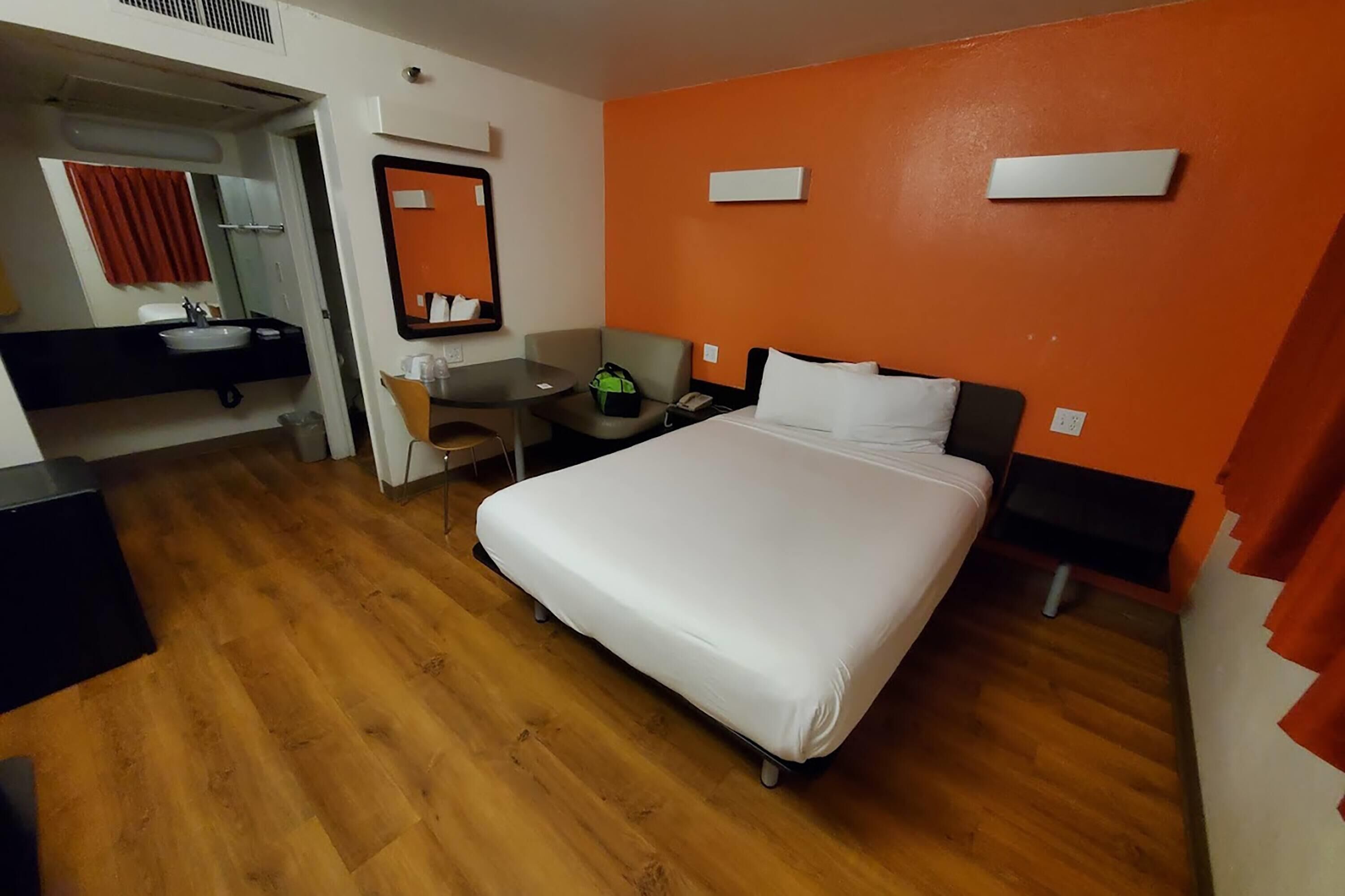A hotel room with a bed, bedside tables, a desk, a chair, a mirror, and a bathroom with a sink and toilet.