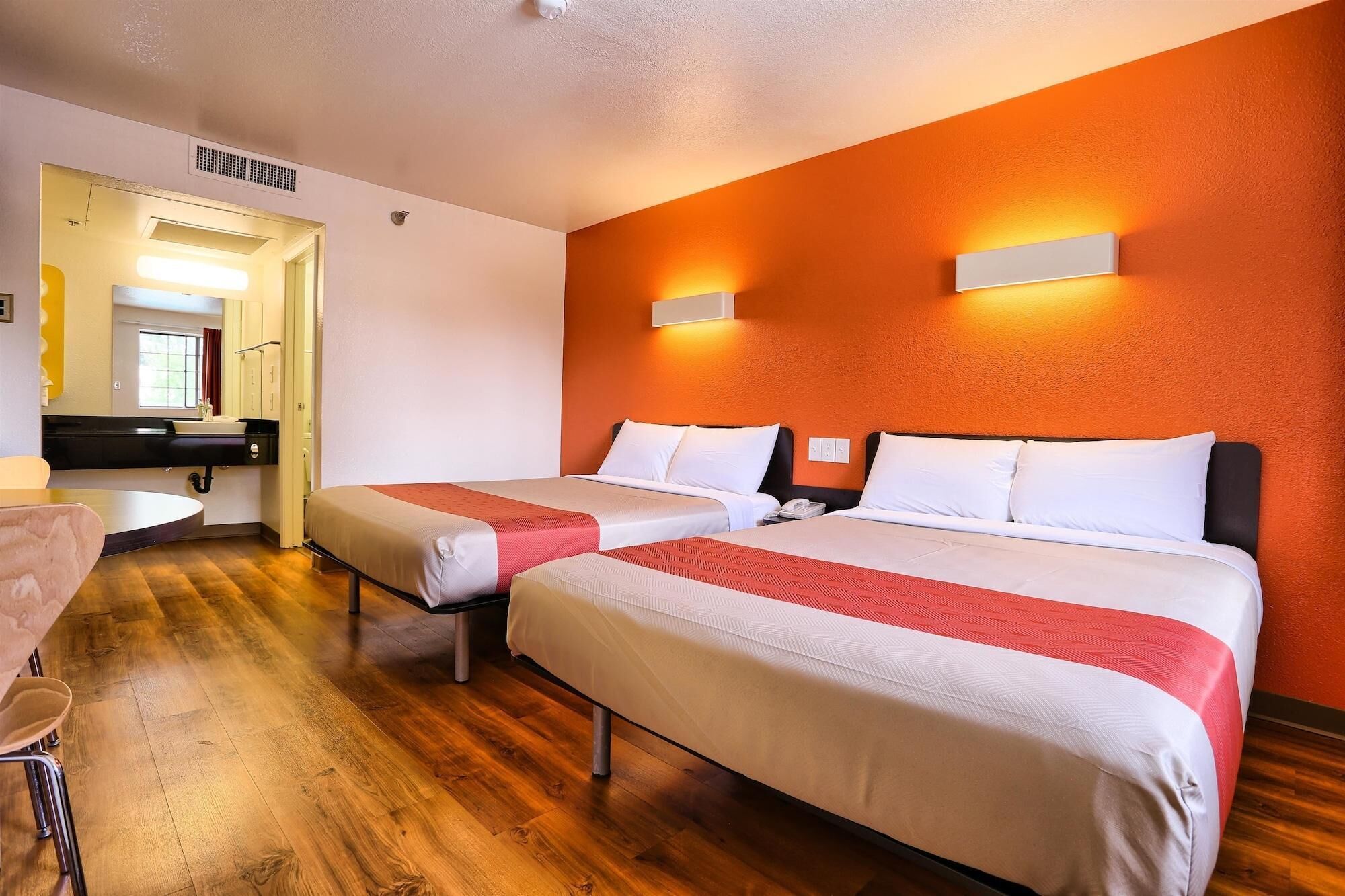 A hotel room with two beds, a small kitchenette, a bathroom, and a dining area.