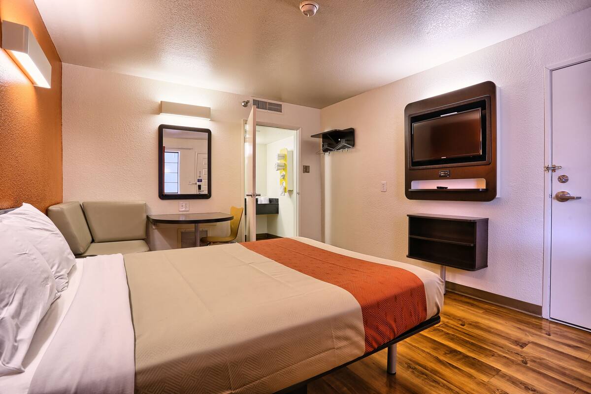 A hotel room with a bed, a TV mounted on the wall, a small table, and a chair.