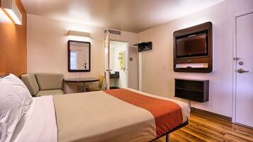 Quarto de hotel com cama, televisão na parede, mesinha e uma cadeira.
