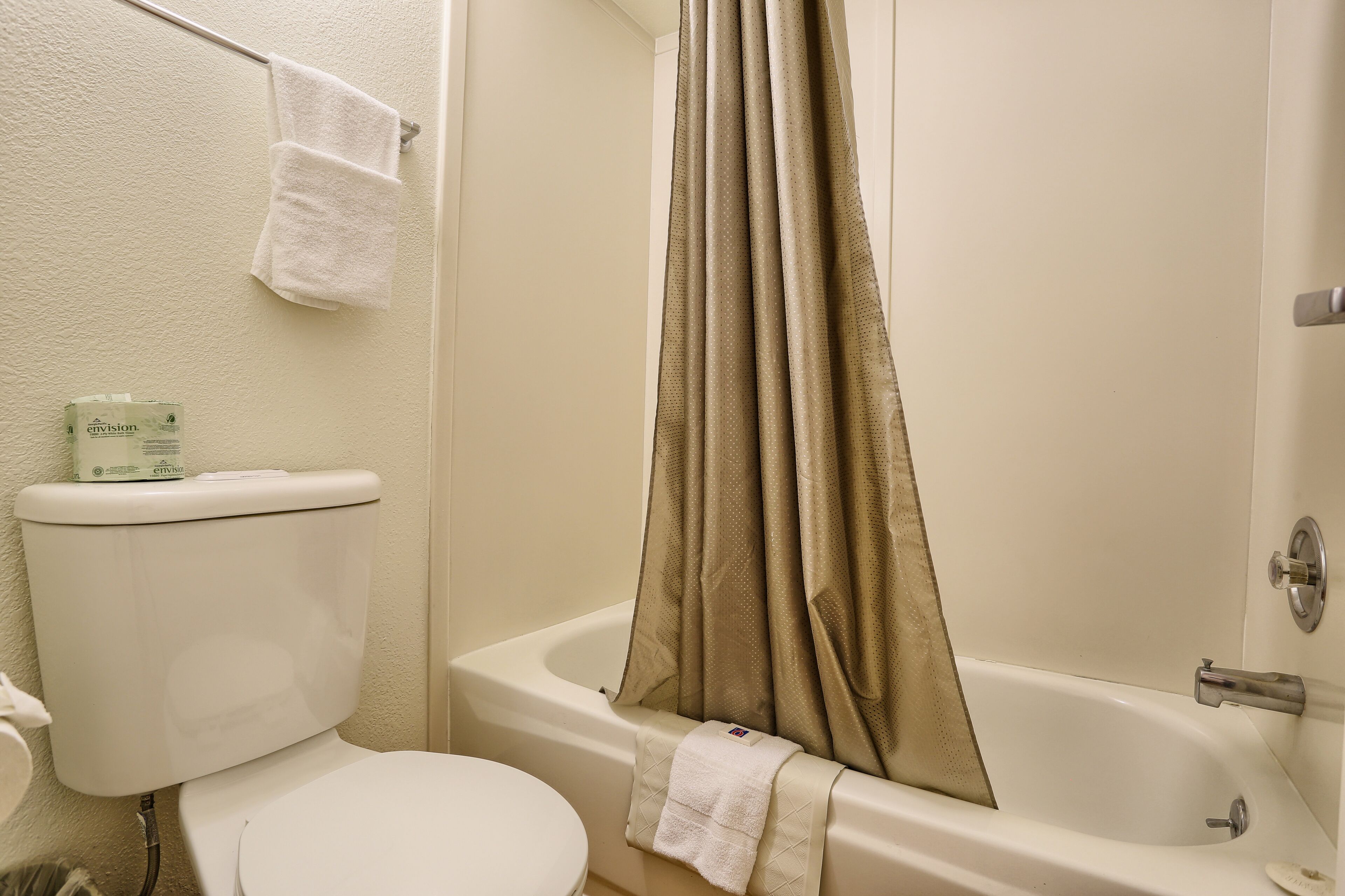 Un baño con inodoro, bañera con cortina de ducha color beige y una toalla colgada en la pared.