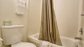 Un baño con inodoro, bañera con cortina de ducha color beige y una toalla colgada en la pared.