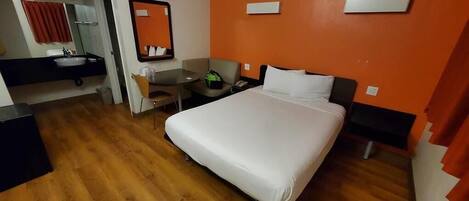 Une chambre d’hôtel avec un grand lit, un bureau avec une chaise, une petite table, un miroir et une salle de bain équipée d’un lavabo et de serviettes.