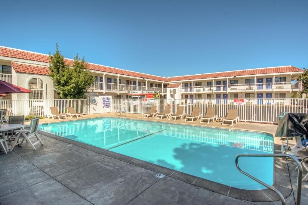 A hotel with a swimming pool, outdoor seating, and a fenced area.
