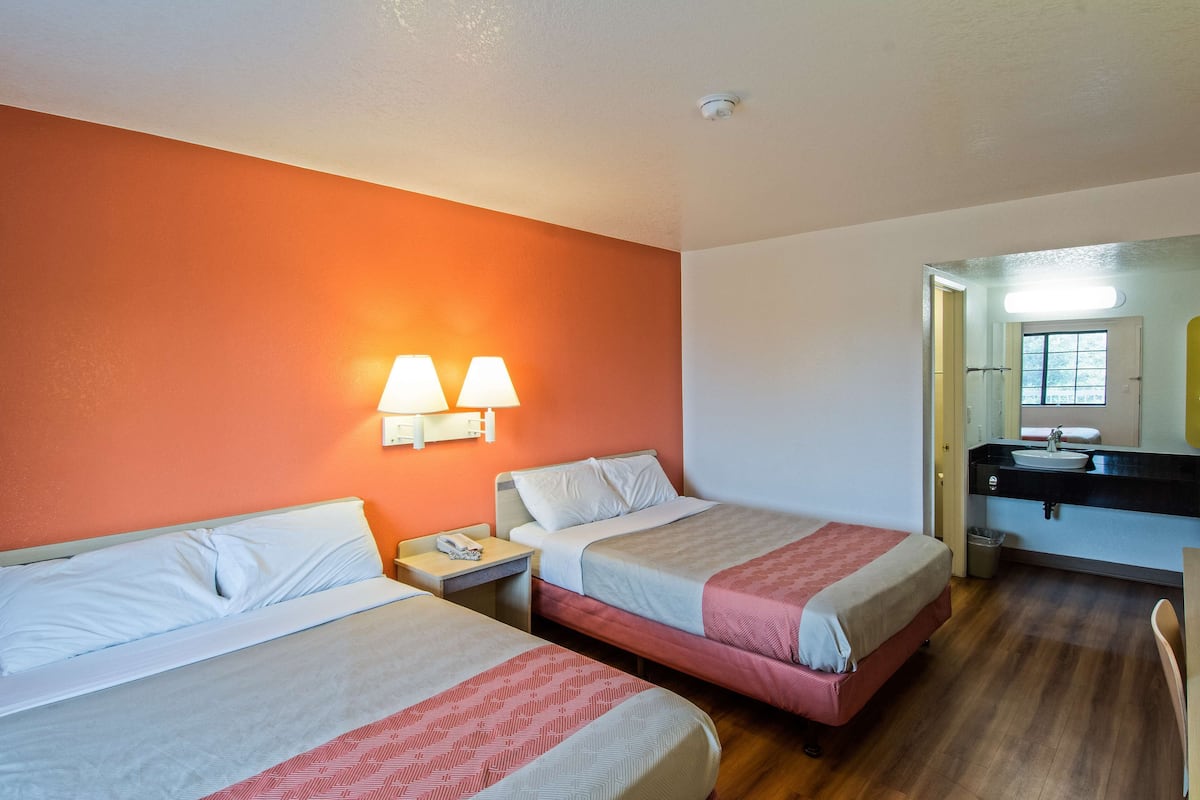 Une chambre d’hôtel avec deux lits, une salle de bain avec un lavabo et un miroir.