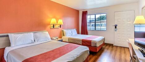 A hotel room with two beds, a desk, a chair, and a window with a view of a building.