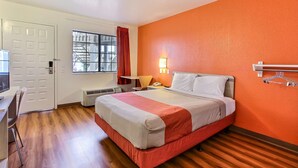 A hotel room with a bed, a desk, a chair, a window with curtains, a wall-mounted heater, and a wall-mounted light fixture. - Motel 6 Salinas, CA - North Monterey Area (Salinas)