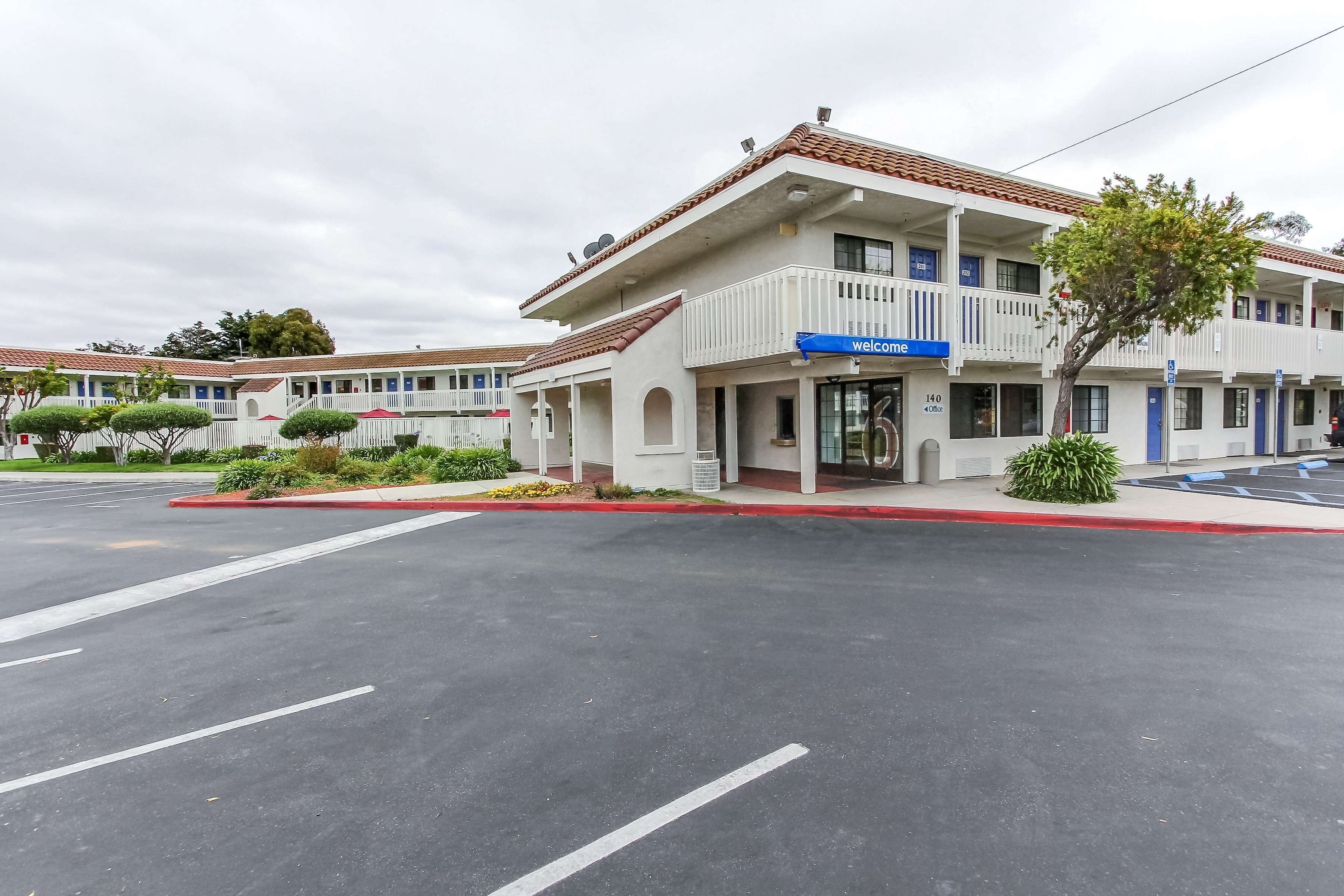 A motel with a 'Welcome' sign, a covered parking area, and a red curb.