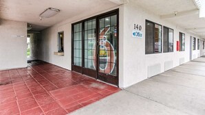 A corridor with a red-tiled floor, a glass door with a metal grid, and a sign indicating room number 140. - Motel 6 Salinas, CA - North Monterey Area (Salinas)