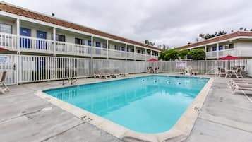 Un motel con piscina, varios balcones y un área vallada con sillones de descanso.