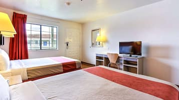 Habitación de hotel con dos camas, un escritorio con televisor, una silla y un ventanal con cortinas rojas.
