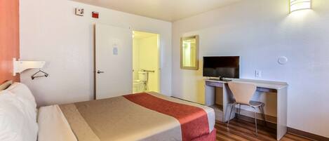 Una habitación de hotel con cama, escritorio, silla, televisor y espejo.