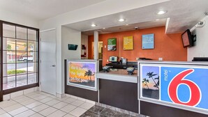 A hotel reception area with a reception desk, a large sign for the number 6 motel, and a view of the outside through a glass door. - Motel 6 Salinas, CA - North Monterey Area (Salinas)