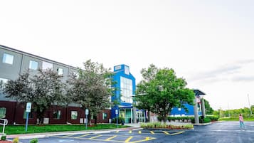 A building with a blue and gray facade, a parking lot with marked spaces, and a pedestrian crossing.