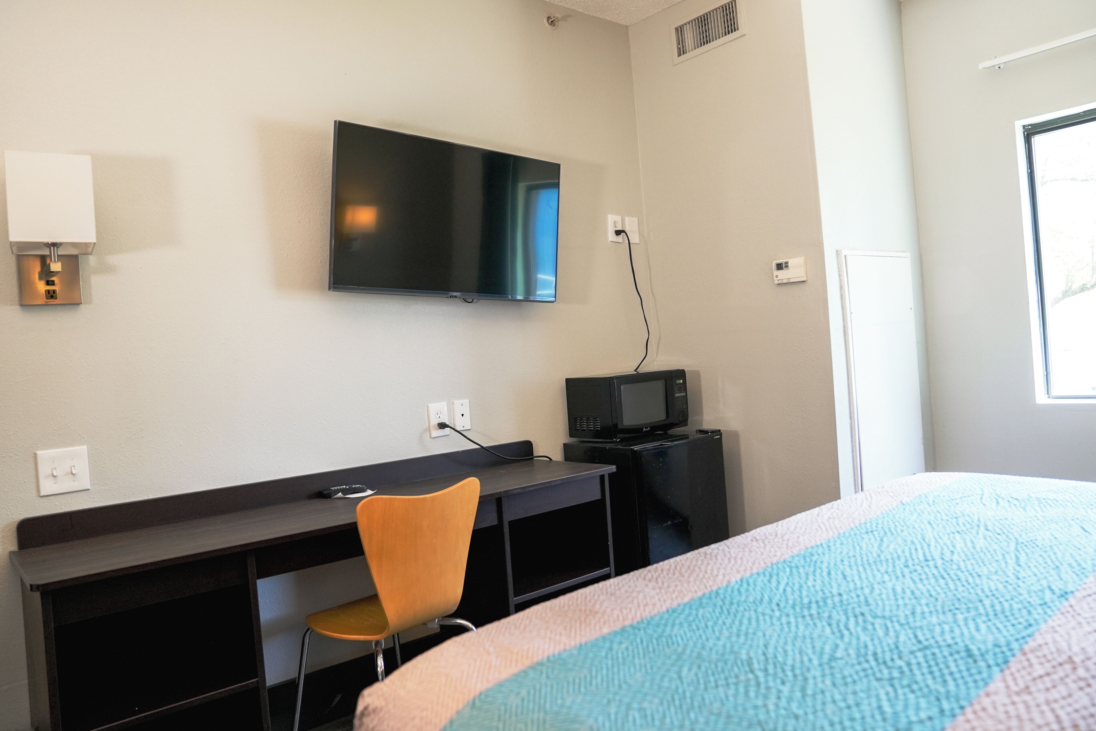 A hotel room with a bed, a desk with a chair, a television, and a microwave.