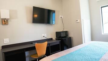 A hotel room with a bed, a desk with a chair, a television, and a microwave.